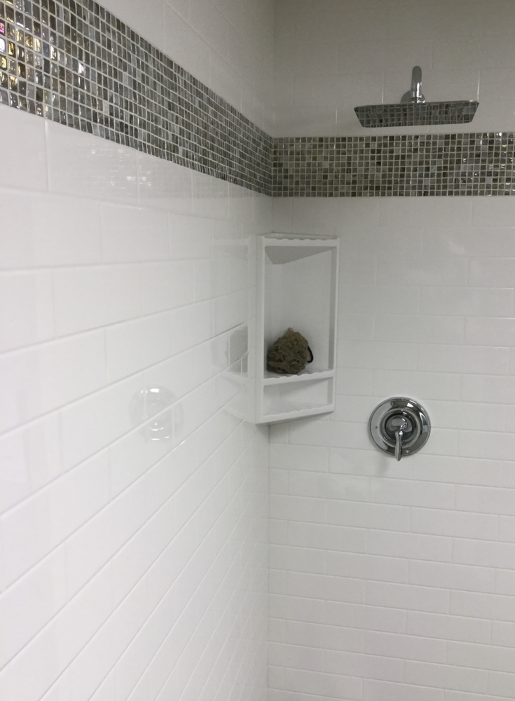 Solid surface shower panels with a subway tile pattern and a decorative glass tile border | Innovate Building Solutions