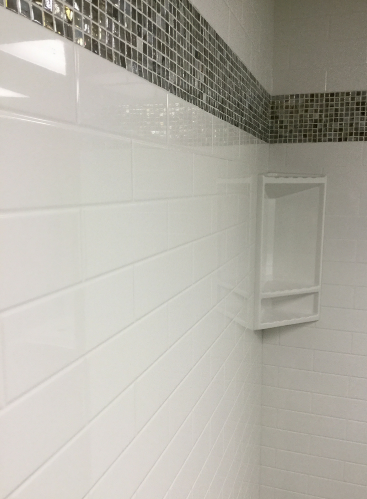 A multicolored glass tile border in a solid surface wall with a subway tile pattern | Innovate Building Solutions 