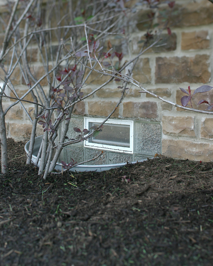 An obscure glass block basement window in a well with an air vent for maximum privacy | Innovate Building Solutions 