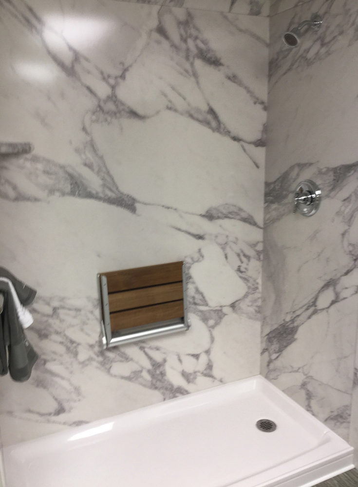 Faux marble calcutta white shower wall panels with an acrylic shower pan and a fold down teak shower seat | Innovate Building Solutions