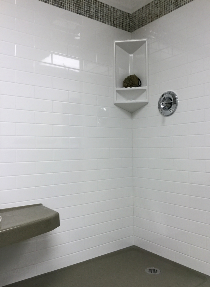 White subway tile solid surface wall panels with an olive colored shower low profile shower pan and an extended corner bench seat | Innovate Building Solutions