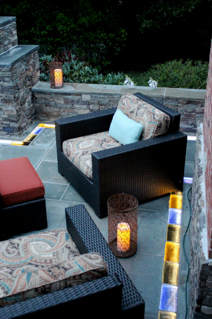 This outdoor fire pit and seating area used decorative blue stone and illuminated colored glass brick pavers for a fun and unique look! | Innovate Building Solutions