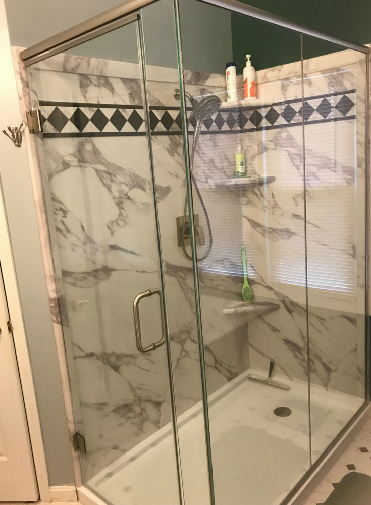 Calcutta white marble faux stone wall panels with a double threshold solid surface shower pan with a frameless 2 sided custom glass enclosure | Innovate Building Solutions 