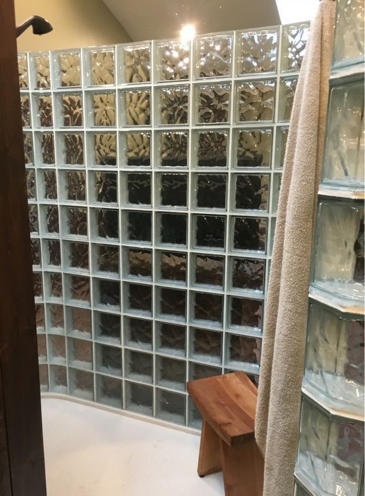 Custom glass block shower on a solid surface base with a teak seating area - Innovate Building Solutions