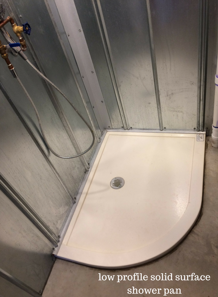 Arc shaped low profile solid surface shower pan in a downstairs shower with exposed plumbing | Innovate Building Solutions 