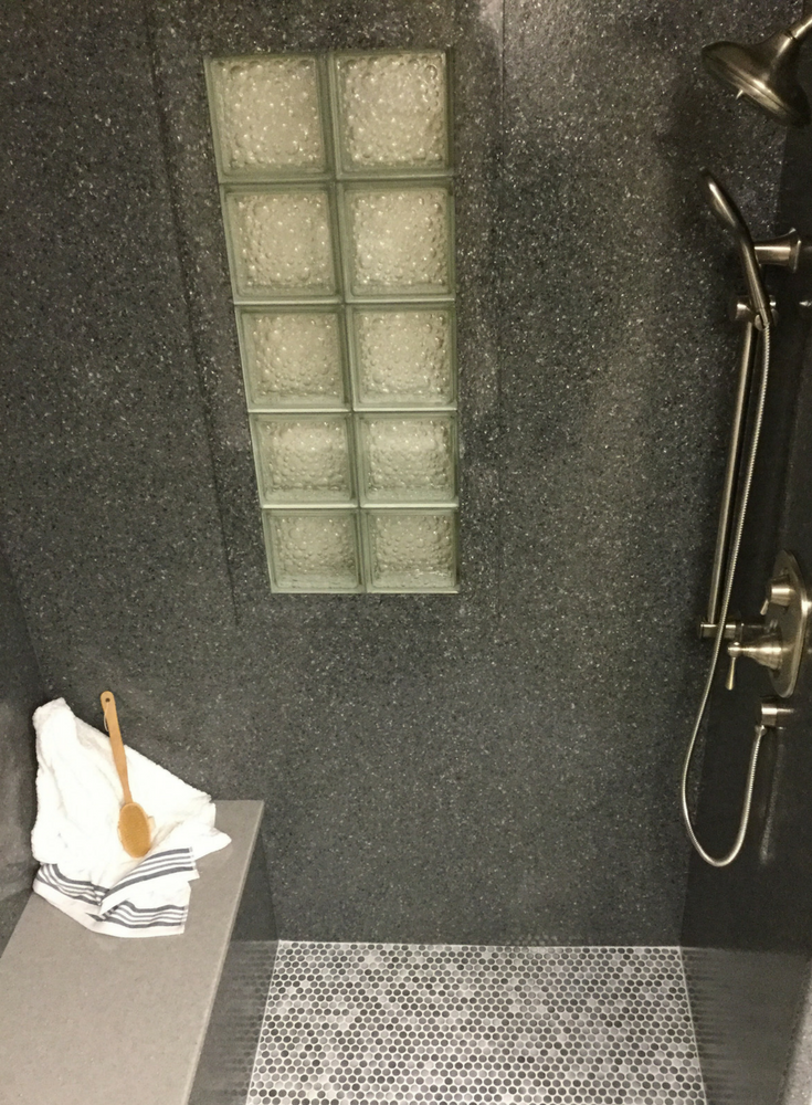 Gray solid surface shower walls and a bench seat in a slate texture with a bubble pattern glass block shower window | Innovate Building Solutions