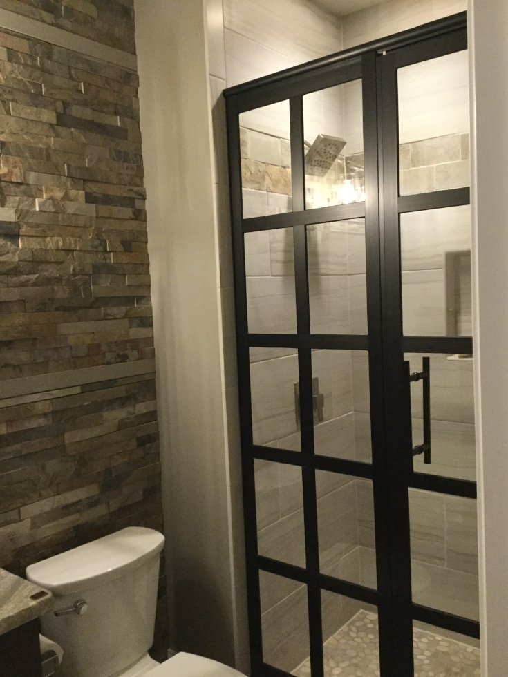 Black framed shower doors in an organic bathroom | Innovate Building Solutions | #ShowerDoors #BathroomTrends #StylishBathroom