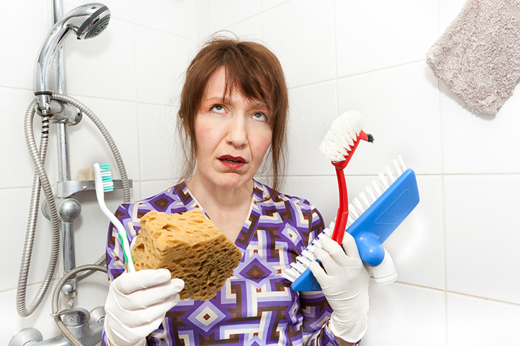 woman with scrub brushes hating tile shower | Innovate Building Solutions | #BathroomRemodel #CleaningGrout #ScrubbingTile